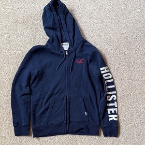 Hollister Navy Zip Hoodie with Red Logo and White Sleeve Text